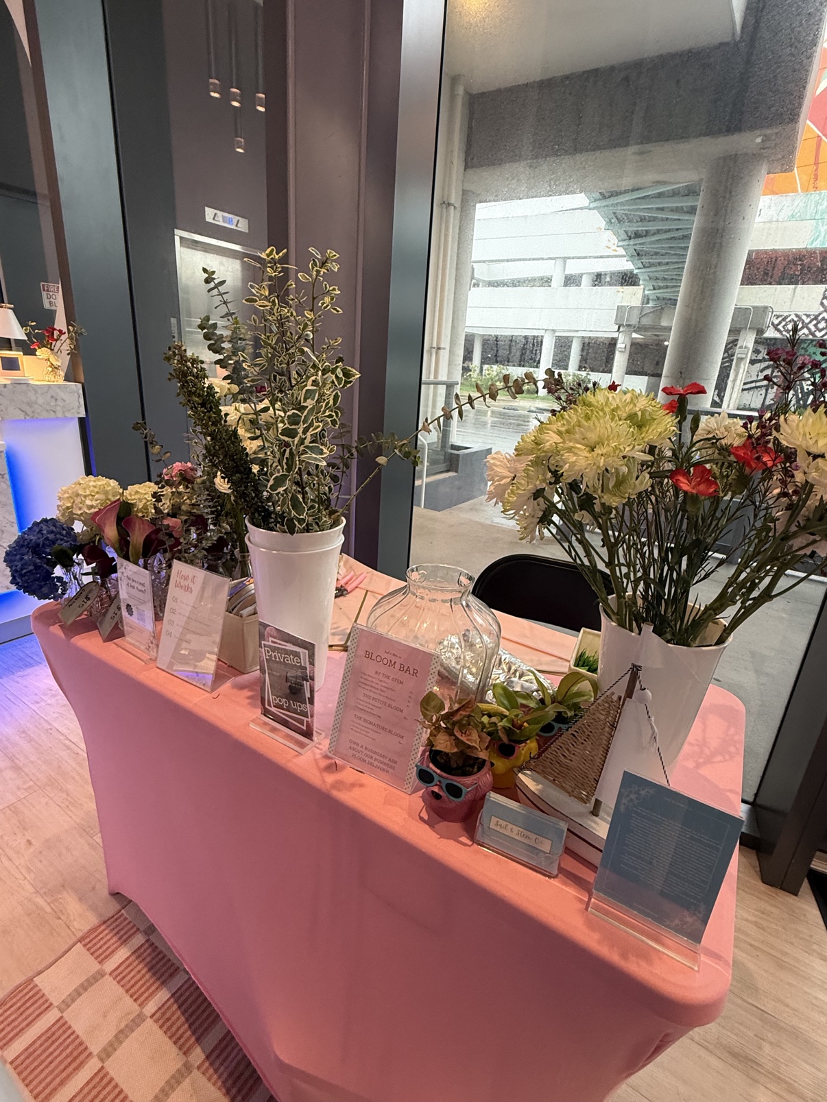 Pink-draped bloom bar table with flowers, greenery, and display cards