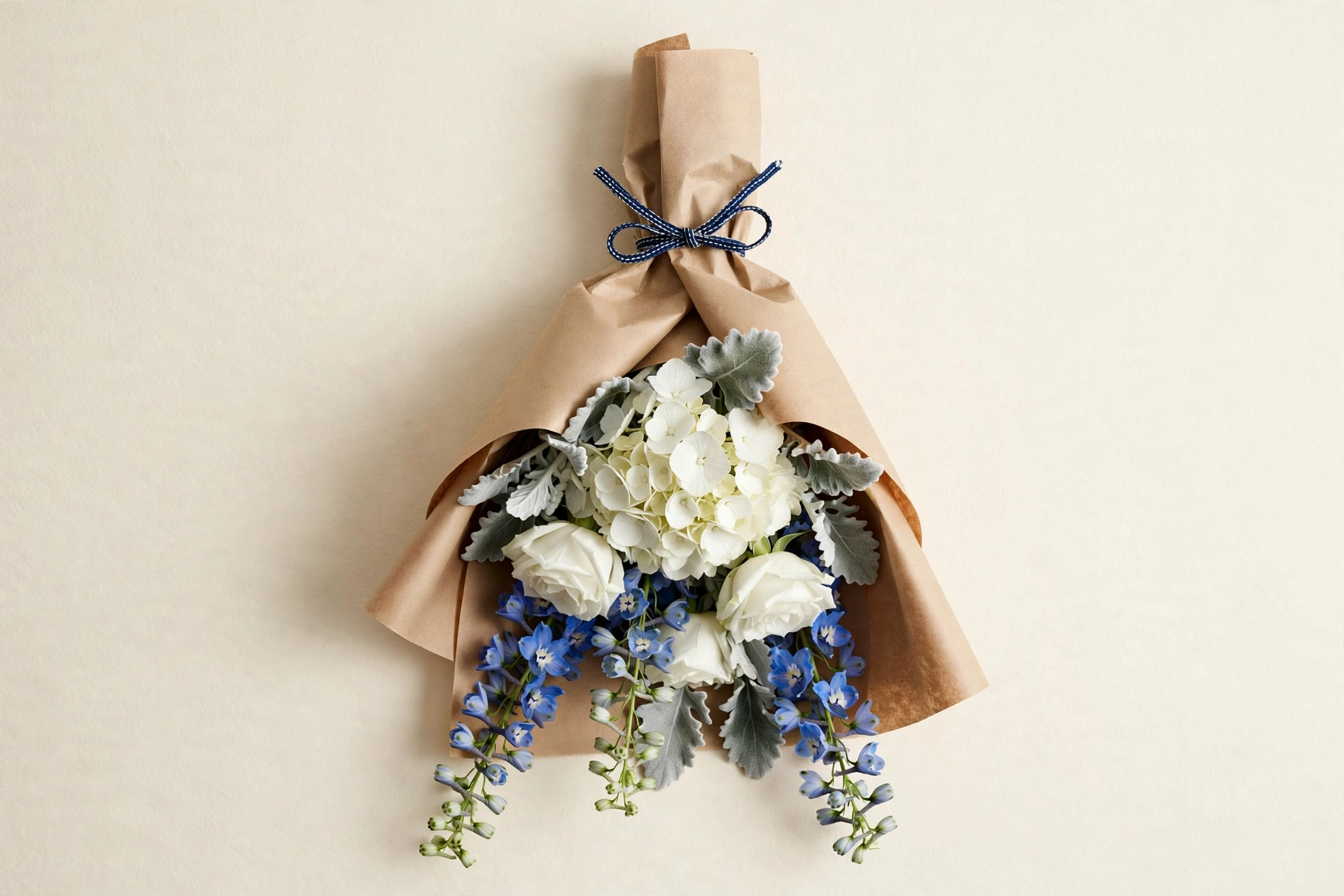 White hydrangeas, white roses, blue delphinium, and dusty miller in a hand-tied bouquet