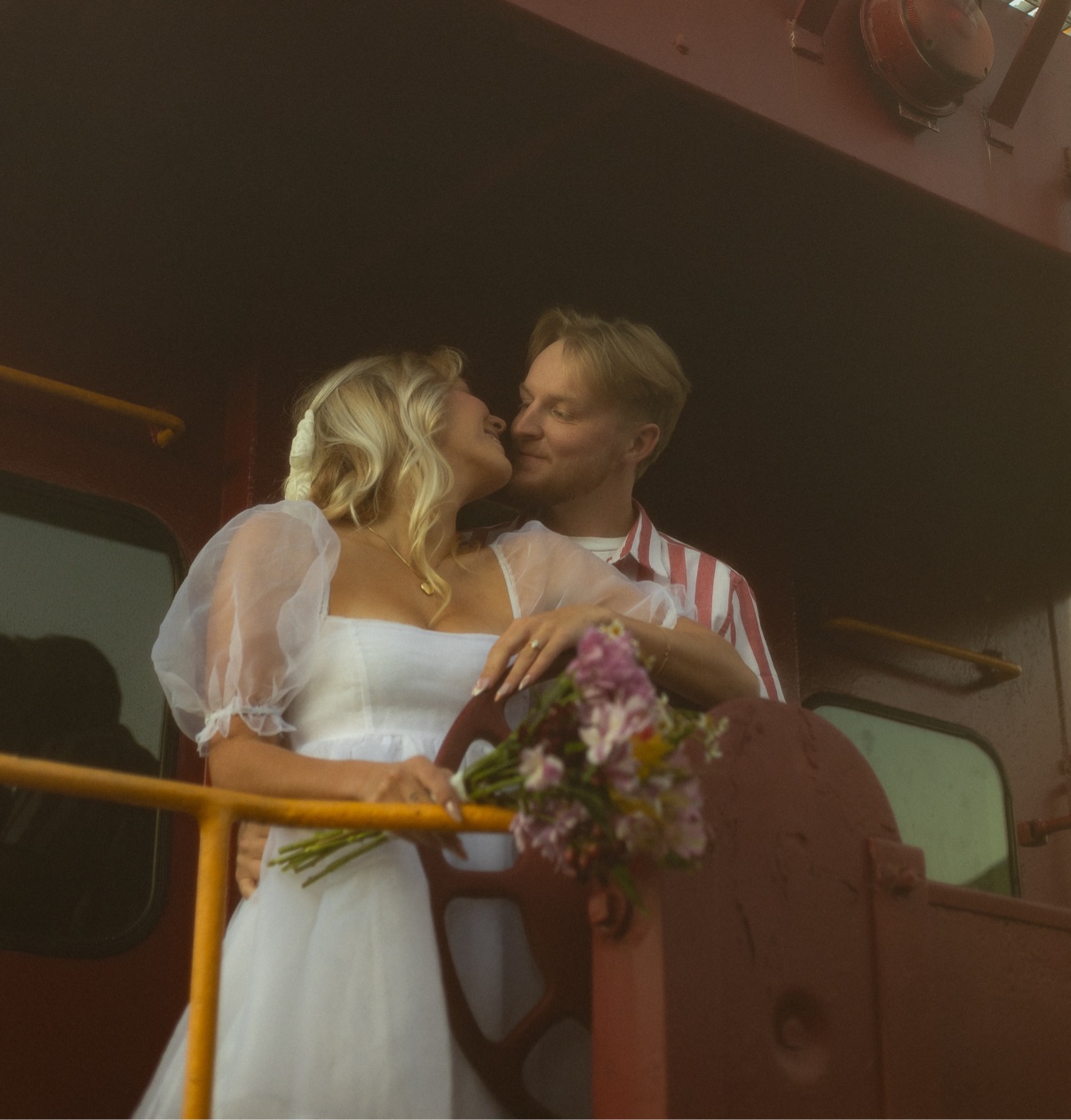 Newlyweds holding a pink and purple bouquet on a vintage train