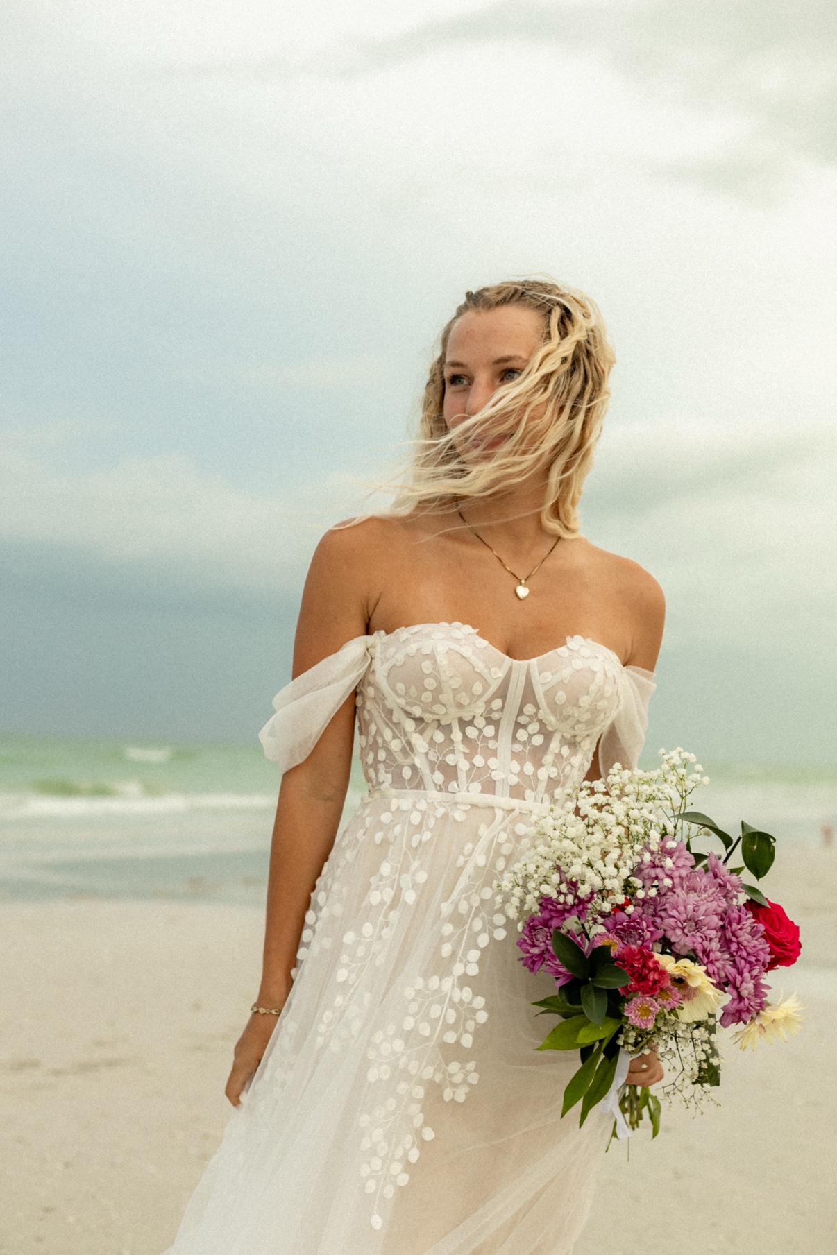 Bride on the beach holding a colorful bouquet of baby's breath, chrysanthemums, and roses